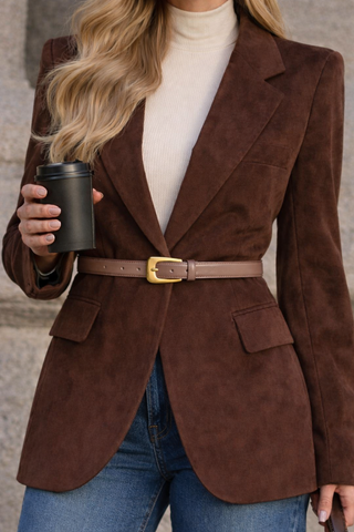Person wearing a brown blazer with a belt, holding a black coffee cup against a neutral background